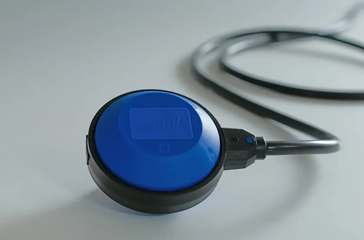 Small pintakytkin | Kaveko Blue circular medical device with a black rim and attached cable on a white surface (close-up).